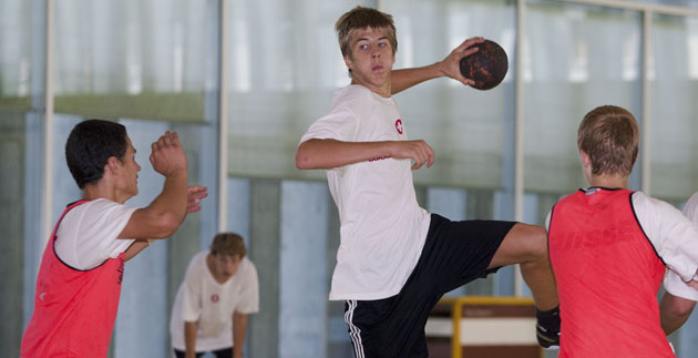 Handball: Jenseits aller Klischees Ein Spieler führt einen geprungenen Angriff über zwei Verteidiger hinweg aus.