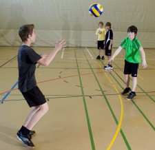 Zwei Kinder werfen sich einen Ball zu, während sie von anderen beobachtet werden.