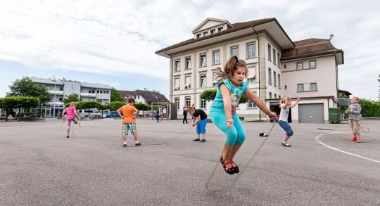Des enfants sautent à la corde dans une cour d'école.