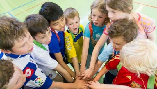 Des enfants sont en cercle tendent leur main vers le centre.