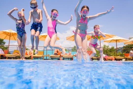 Kinder springen im Schwimmbad ins Wasser.