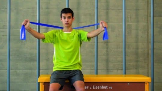 Un jeune effectue un exercice de force assis sur un banc suédois.