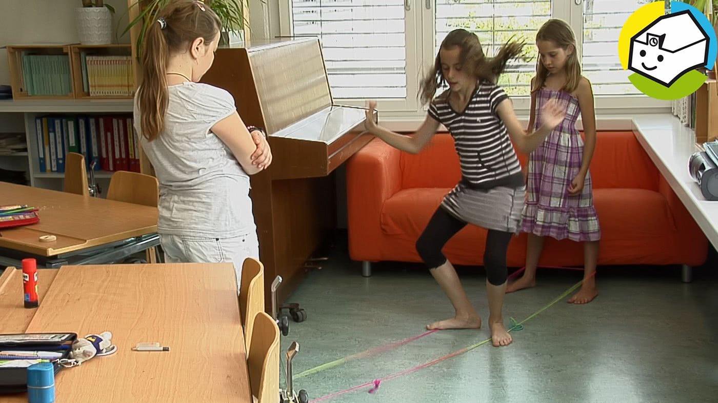 Drei Mädchen beim Gummitwist im Schulzimmer.