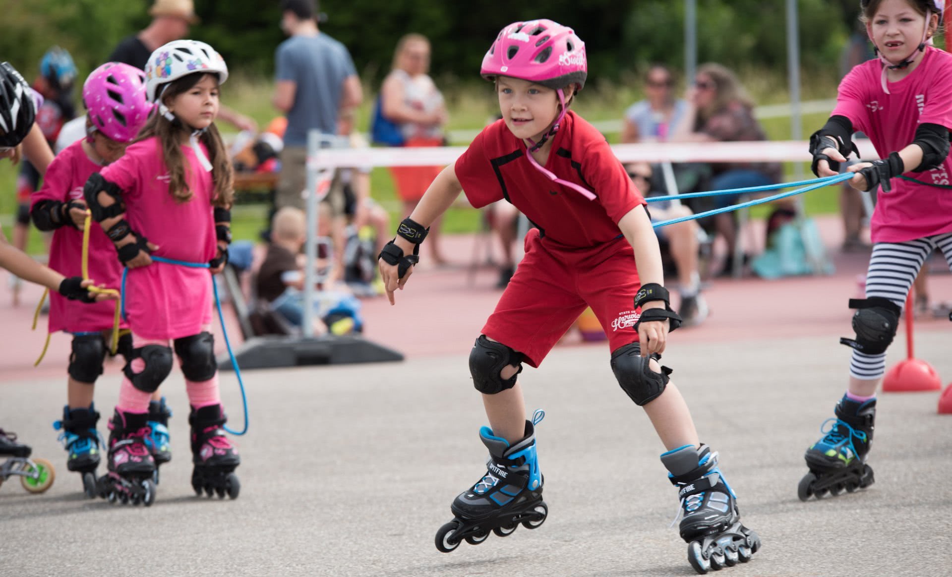 Ein Mädchen auf Inline-Skates zieht ein anderes mit einem Seil.
