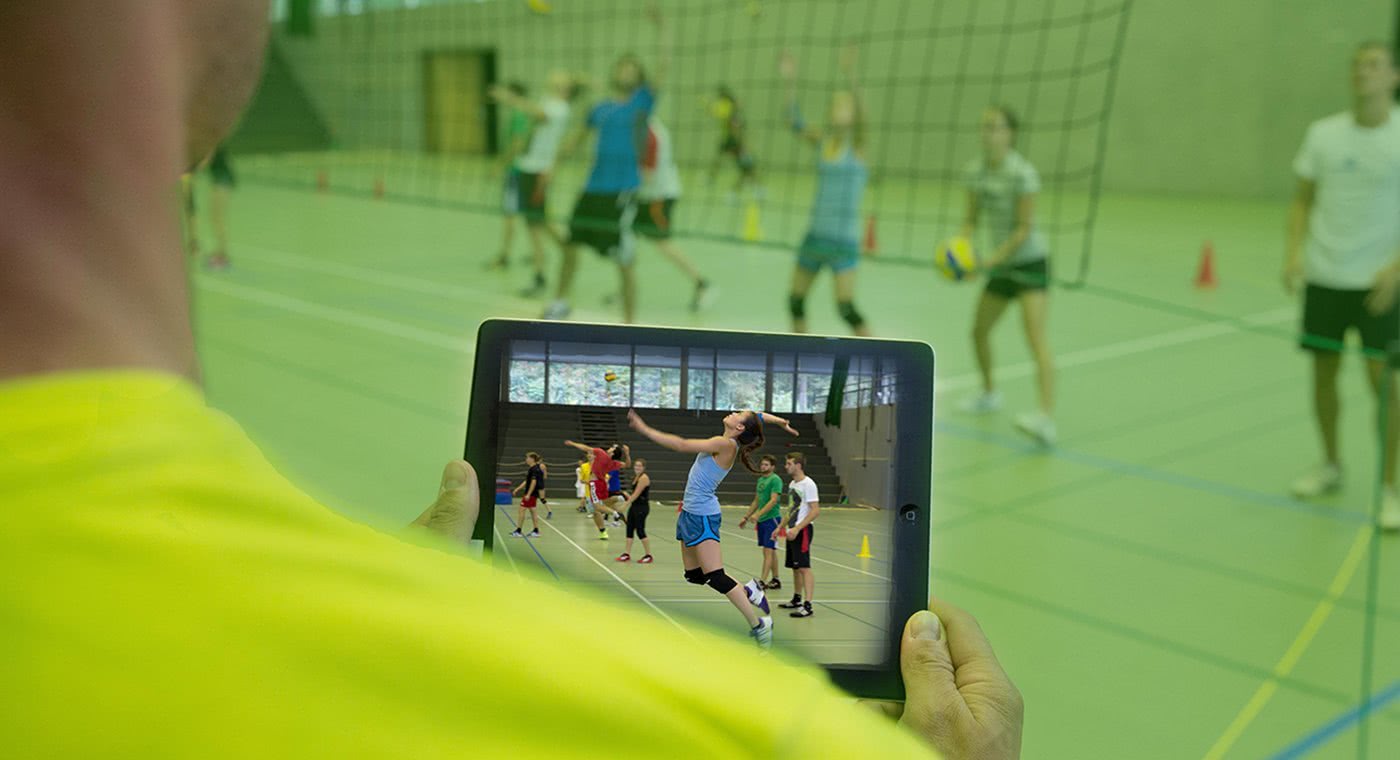 Trainer schaut auf I-Pad und vergleicht Soll- und Ist-Bilder von Athletin.