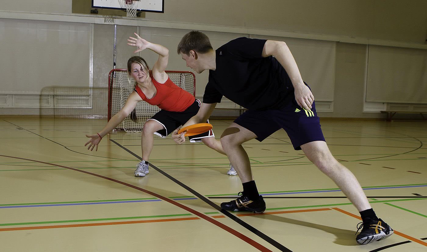 Junge Frau und junger Mann spielen Frisbee auf Unihockey-Tor.
