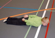 Un bambino sdraiato per terra con la testa sollevata e le mani dietro la schiena