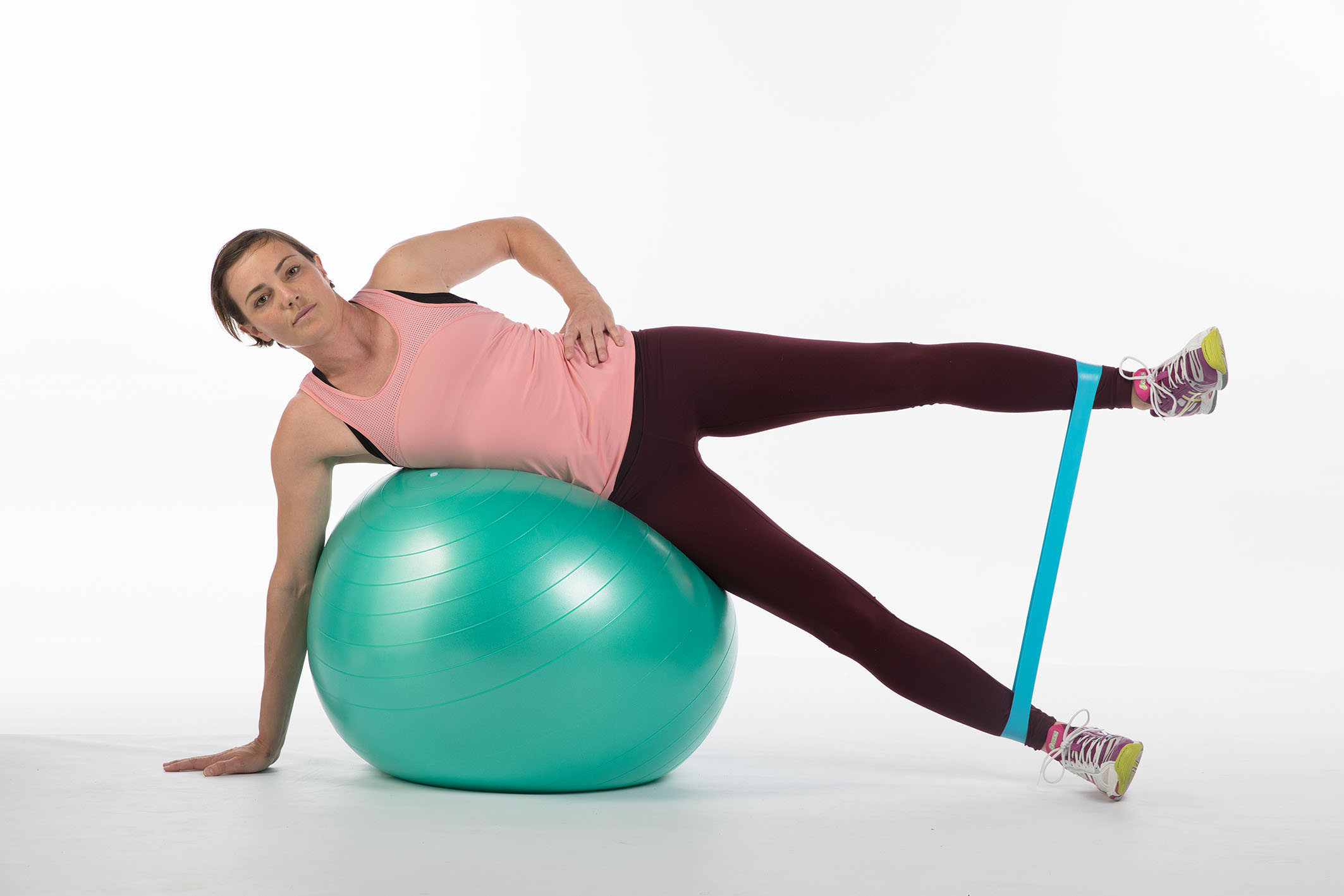 Foto: Eine junge Frau liegt seitwärts über einen Swissball, mit einem Miniband um die Knöchel