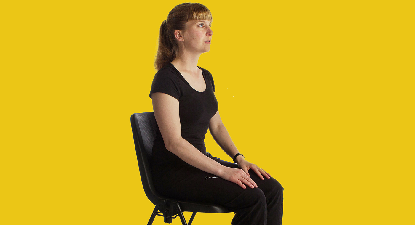 Assise sur une chaise, une dame effectue un exercice de relaxation.