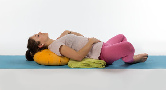 Una ragazza è sdraiata sulla schiena, appoggia le spalle su un cuscino, ha le gambe piegate e gli occhi chiusi