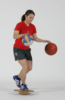 Agrandir l'illustration: Entraînement proprioceptif: Eveil sensoriel garanti Une athlète est en équilibre sur un ballon et fait rebondir un ballon de basketball et un ballon de volleyball.